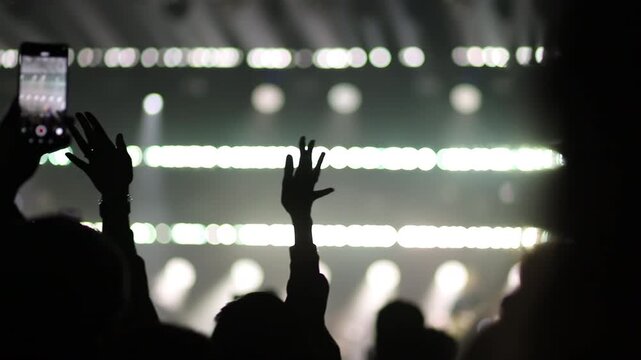Crowd at music concert with hands raised and cell phone recording stage. Live event with people celebrating and engaging with performance.