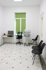 Interior of an ophthalmologist's office with a slit lamp biomicroscope, a table with a laptop and two chairs.