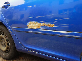 Scratched or grazed car door body panel with damaged paint job and rusty panel after minor accident. Low angle, close up shot, no people