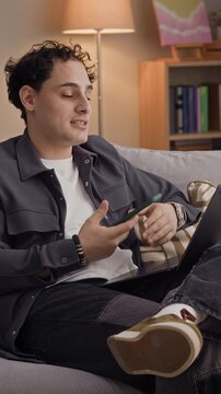 Vertical shot of curly haired man showing smartphone screen to friend while chatting with him during video call