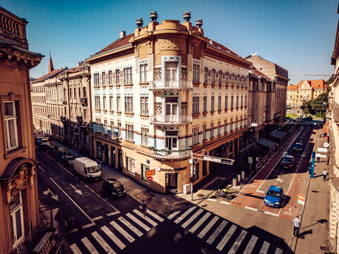 Aerial view of a sun-drenched corner building with ornate balconies overlooks a vibrant street scene with its painted bike lanes, Zagreb, Croatia.