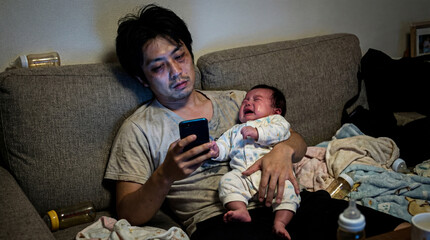 深夜に泣く赤ちゃんを抱えながらスマホを見る日本人の父親