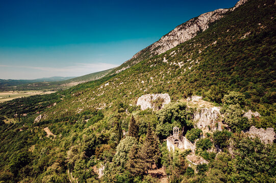Aerial view of verdant trees clinging to the rugged mountainside, ancient stone ruins nestled amidst the dense forest, a vivid contrast against the clear blue sky, Pican, Istria County, Croatia.