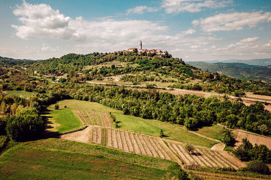 Aerial view of a hilltop settlement with a church steeple rising above the green landscape and cultivated fields, Pican, Istria County, Croatia.