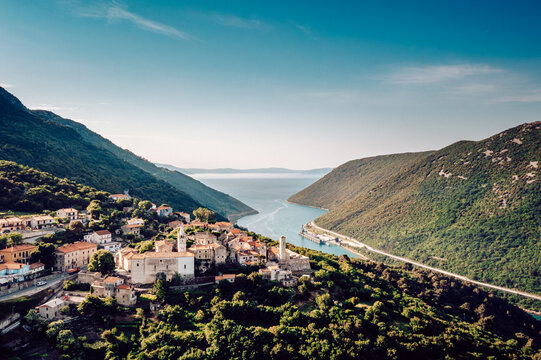 Aerial view of the charming village nestled amidst lush hills, overlooking the serene bay under a clear sky, Pican, Istria County, Croatia.