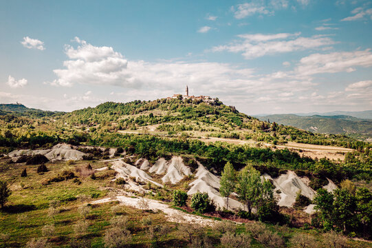 Aerial view of a medieval hill town crowned with a tall church tower and surrounded by verdant hills under a vast sky, Pican, Istria County, Croatia.