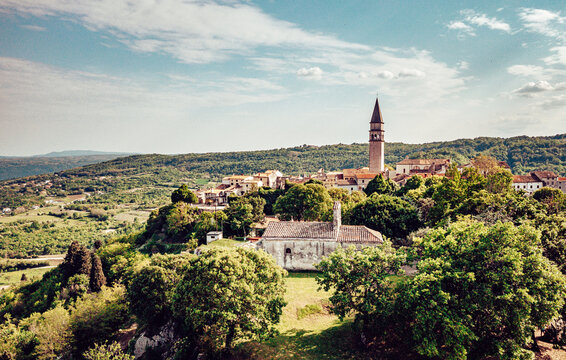 Aerial view of the ancient town with the towering steeple of the Church of St. Michael the Archangel piercing the skyline, amidst a tapestry of verdant trees, Pican, Istria County, Croatia.