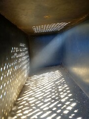 Inside a dark, rectangular space with light filtering through holes in the ceiling and wall