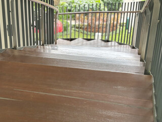 High-angle view of a modern curved outdoor wooden staircase with metal handrails, leading down to a lush green landscaped garden area on a bright sunny day.