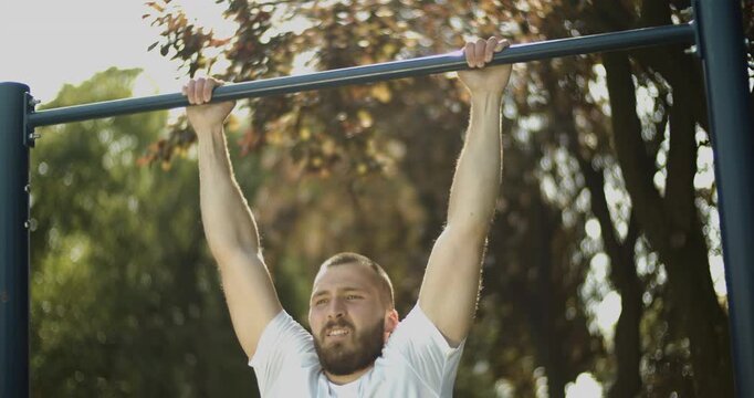 Young athlete performs pull up exercise  outdoors, street workout, slow motion, middle close up 