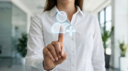 Woman in white shirt tapping virtual add user icon with finger in bright office, confident gesture and modern interface