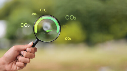 Hand Holding Magnifying Glass Checking Low CO2 Emission Gauge for Sustainability