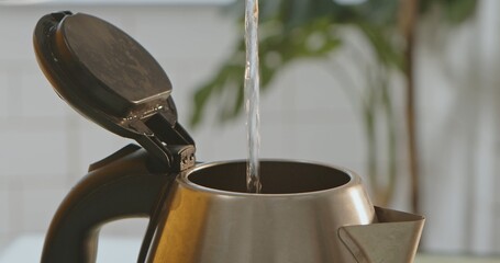 Close up view of water being poured into an open electric kettle, with a blurred background. Ideal...
