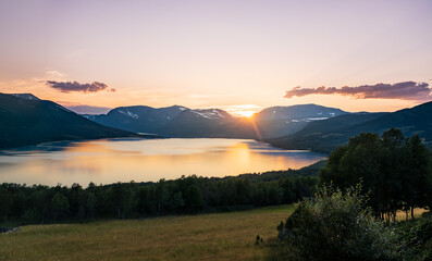 Sun sets over Gjevillvatnet lake. The scene shows Bl&aring;h&oslash;a and Gjevilvasskamben mountains in the Trollheimen range in Oppdal Norway. Evening light reflects on the water.
