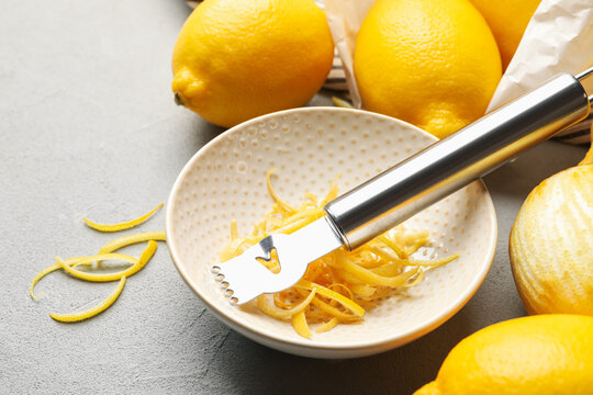 Fresh lemons with zest and zester tool on grey table, closeup