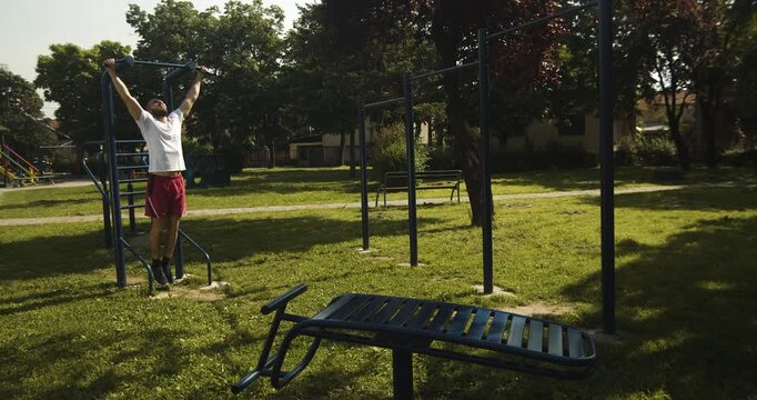 Athlete performs pull up exercise on outdoor gym equipment, street workout, slow motion