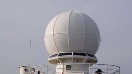 Radar dome located on a ship in a harbor during overcast weather in a calm sea setting