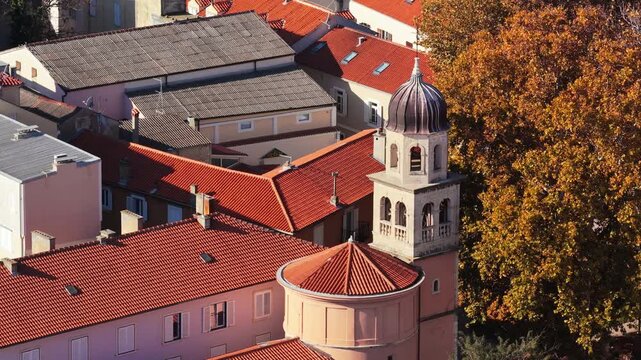 Aerial drone view of a small historic church with a rounded apse and a stone bell tower topped with a dark dome. Zadar, Croatia