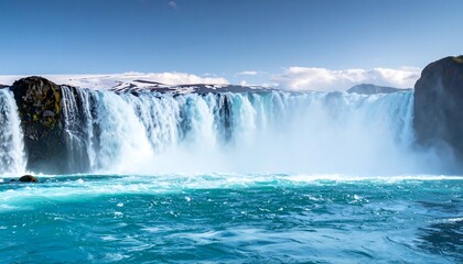 Cascading turquoise waterfall with snowy peaks under a clear blue sky on a sunny day