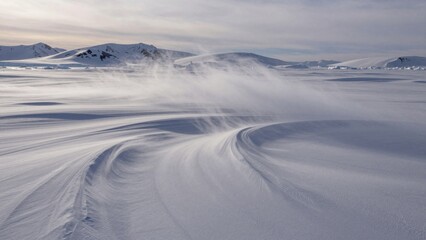 Snow swirls across a vast arctic landscape during winter with distant mountains in the background