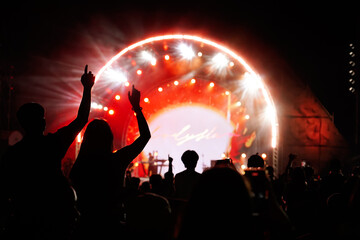 Silhouettes of hand raised of fans in crowd at concert in front of stage with bright spotlights.The back view of people enjoy live music at the band's performance. Outdoor concert.