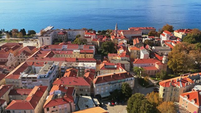 Aerial drone view a cluster of terracotta roofed buildings near the waterfront, with trees and a central plaza. Zadar, Croatia