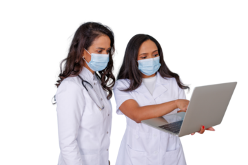 Female doctors in medical scrubs and masks discussing patient data on laptop, consulting in healthcare