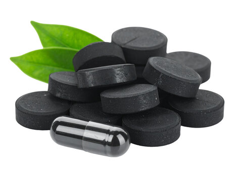 Black charcoal tablets and green leaves isolated on white