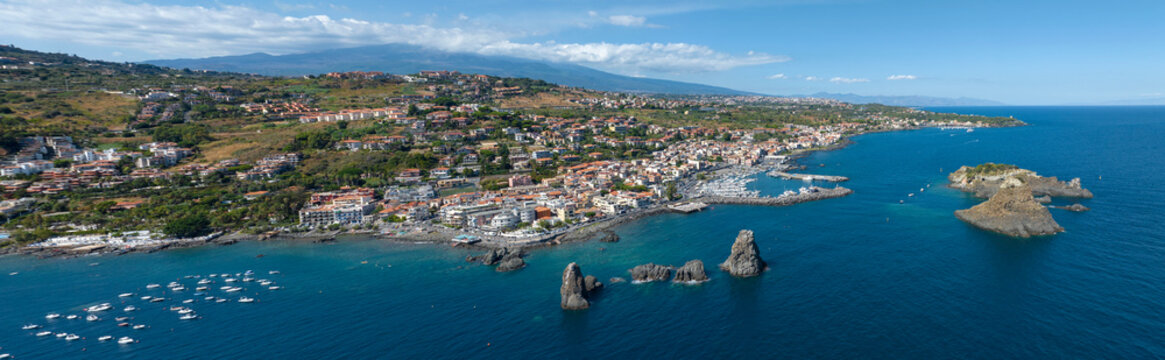 Panoramic aerial view of Aci Trezza, in the province of Catania, Sicily, Italy. It is a tourist resort on the Mediterranean Sea. In the foreground are the Cyclopean Isles. It is a sunny day morning.