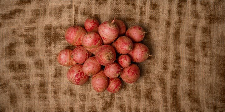 Macro shot of pink oca and yams on textured hessian surface, highlighting root vegetables for food preparation