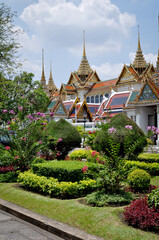 Obraz premium Royal Palace Bangkok. A panoramic view showcasing the intricate rooftops of temples surrounded by blooming foliage