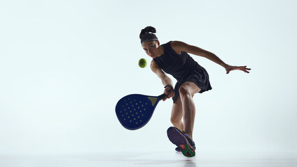 Female padel player reaching low ball with racket in studio. Concept of responsive digital systems, input accuracy, real time interaction and padel training technology.