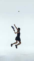 Obraz premium Female padel player jumps mid-air to hit the ball against clean studio background. Concept of marketing campaigns, brand storytelling, dynamic advertising visuals, sports promotion content.