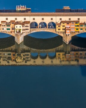 Aerial view of the Ponte Vecchio's ancient stones reflecting in the Arno River's tranquil waters, its shops a testament to time, Florence, Tuscany, Italy.