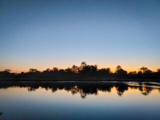 Obraz premium Calm Sunset Over Lake With Tree Silhouettes and Reflection