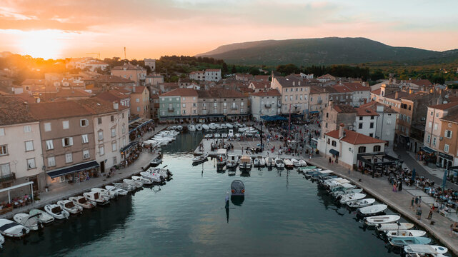 Aerial view of boats nestled in the harbor waters, buildings lining Ulica Riva creskih kapetana under a warm sunset glow, Cres, Primorsko-goranska zupanija, Croatia.