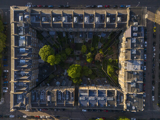 Aerial view of a symmetrical building block surrounds a lush garden oasis, contrasting the rigid architecture with soft greenery, West End, Scotland, United Kingdom.