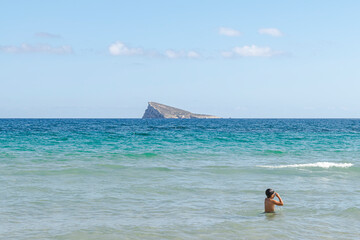Kid standing with swimming goggles in turquoise waves near the shore with a visible island afar in the background on a clear, bright, sunny day.