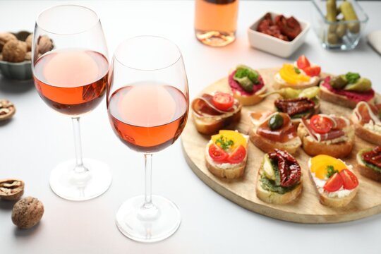 Tasty bruschettas with prosciutto and rose wine served on white table, closeup