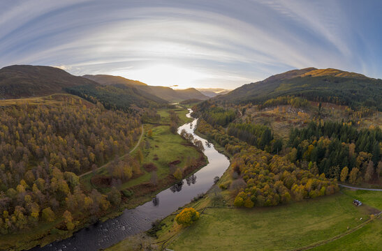 Aerial view of River Tay snakes through a valley of autumnal hues, flanked by forests ablaze in gold, ochre, and russet under a vast sky, Aberfeldy, Scotland, United Kingdom.