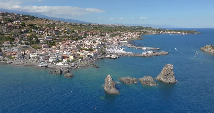 Aerial view of the town of Aci Trezza overlooking the Ionian Sea, in the province of Catania, Sicily, Italy. In the foreground, off the coast, are the Cyclopean Isles. In the background is Mount Etna.