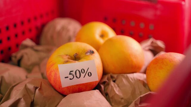 A sticker with a minus 50 percent discount is glued to a slightly rotten apple, close-up. Sale of illiquid goods