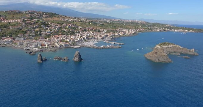 Aerial view of the town of Aci Trezza overlooking the Ionian Sea, in province of Catania, Sicily, Italy. In the foreground, off the coast, there are three tall, characteristic and prominent sea stacks