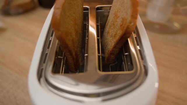 Bread pops out of the toaster and hands pick it up. Making toast, close-up