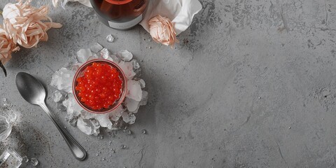 Glass bowl filled with red caviar on ice with a champagne flute on a concrete background, highlighting indulgent presentation