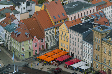 Aerial view of vibrant buildings with terracotta roofs and orange umbrellas casting shadows on the old town square, Stralsund, Mecklenburg-Vorpommern, Germany.