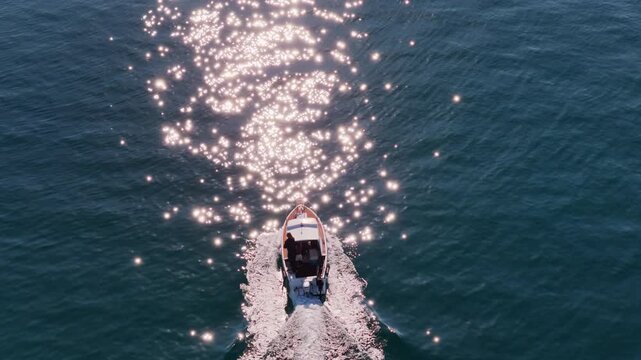 Aerial drone view of a small motorboat speeding across the water, leaving a white foamy trail behind it on the calm turquoise sea. Biograd na Moru, Croatia