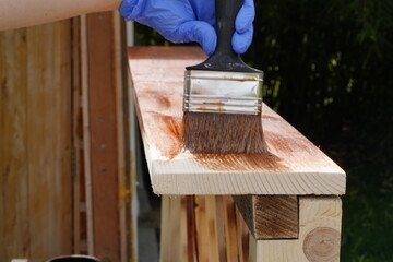 Applying wood stain with paint brush on wooden railing during outdoor renovation