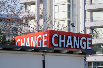 a red rooftop sign featuring the word "CHANGE" repeated in white letters, set against a backdrop of a modern white apartment building and bare tree branches. © Andrey