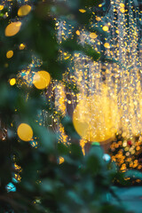 festive blurred lights with green leaves, golden holiday glow defocused through foliage background,...
